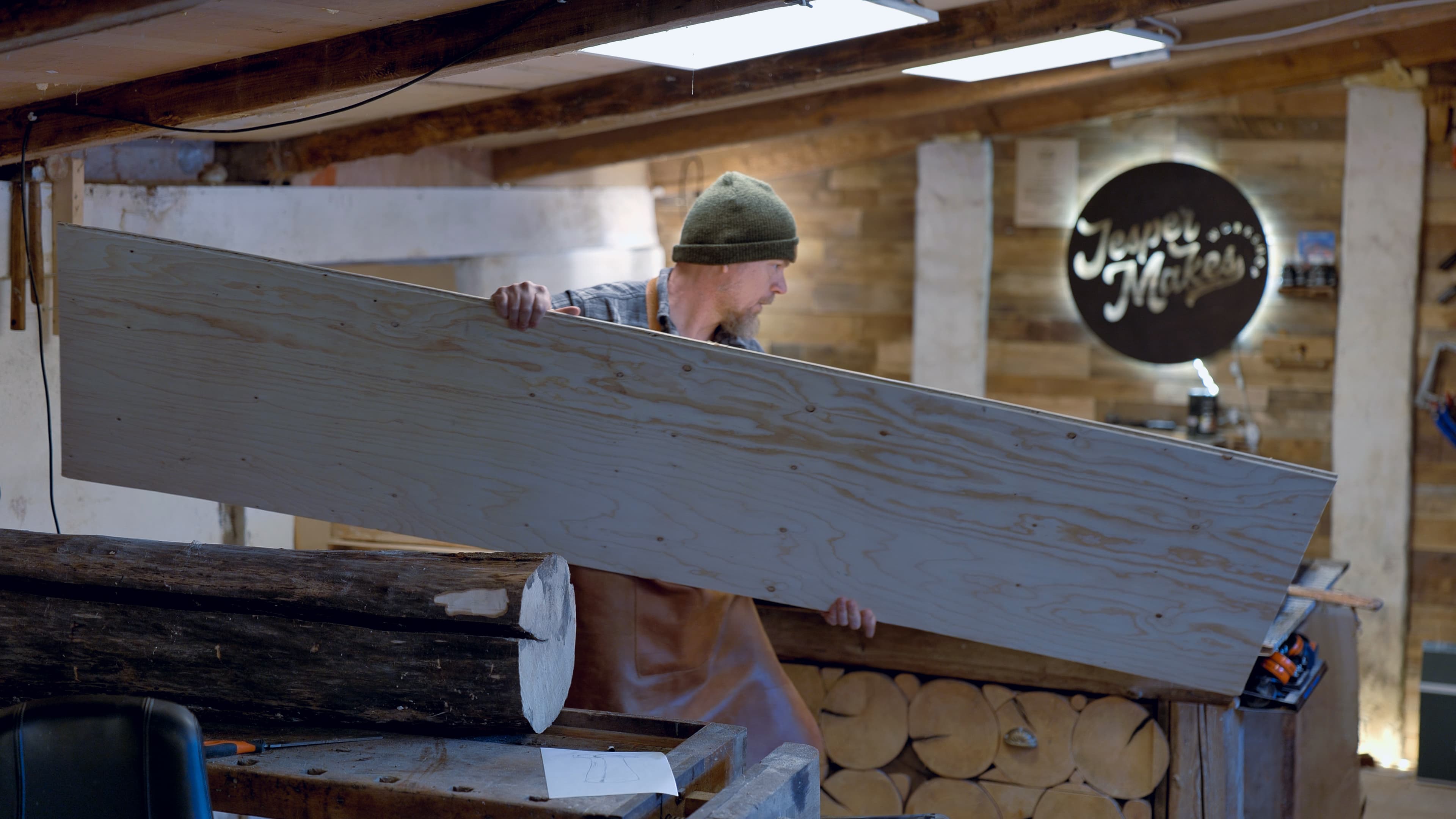 Jesper carrying a board in the workshop, logo sign on wall
